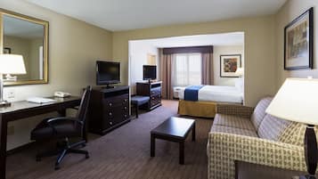 A hotel room with a desk, chair, television, bed, and sofa.
