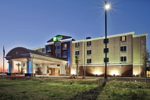 Un hotel Holiday Inn Express & Suites con entrada cubierta, estacionamiento y una farola.