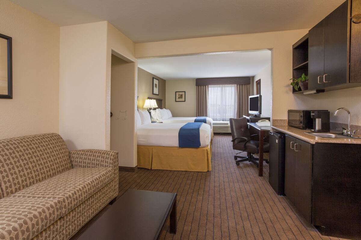 A hotel room with a sofa, a bed with a blue blanket, a desk with a computer, a coffee maker, and a TV.