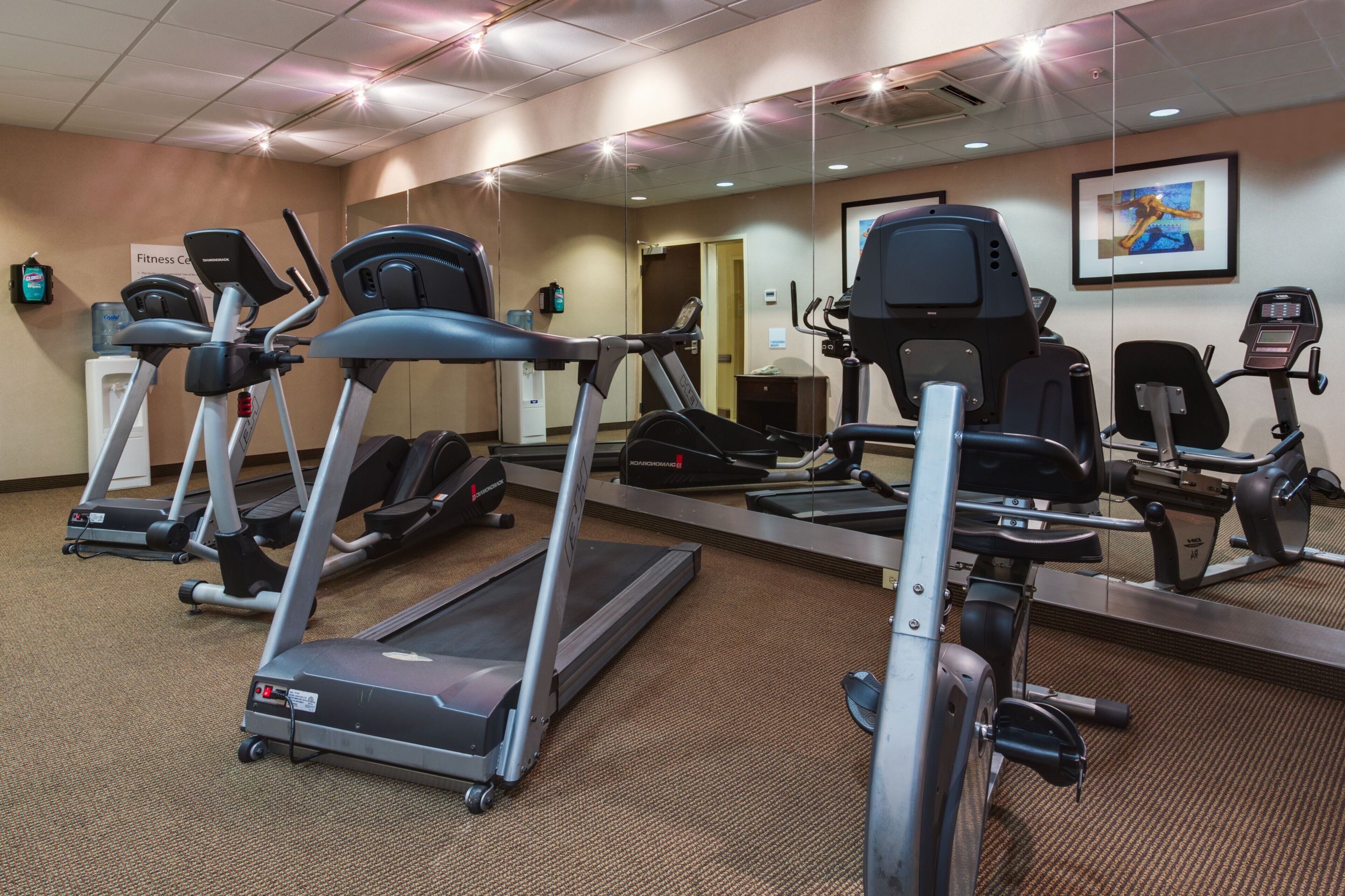 A gym with multiple treadmills, stationary bikes, and a mirrored wall.