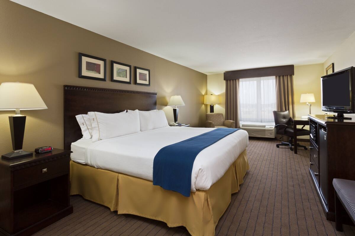 A hotel room with a large bed, bedside tables, a desk with a chair, a television, and framed pictures on the wall.