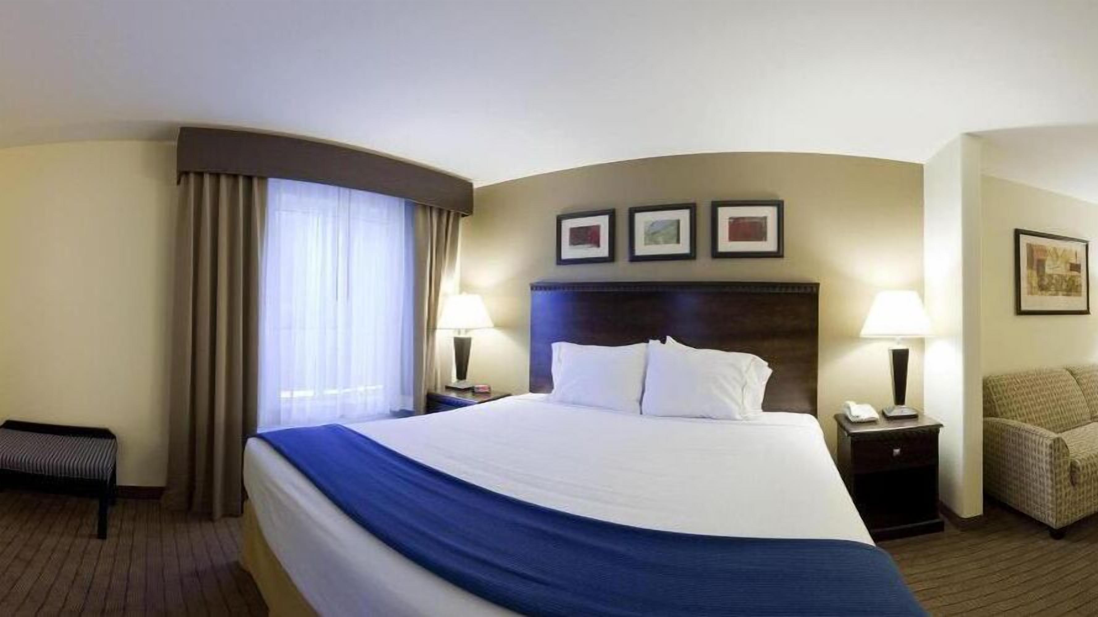 A hotel room with a large bed, two bedside tables with lamps, a chair, and a window with curtains.