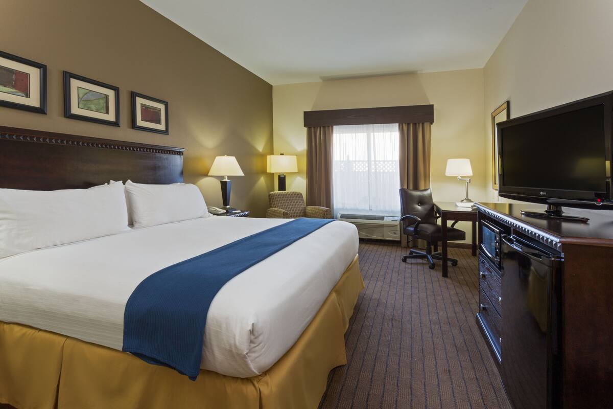A hotel room with a large bed, a desk with a chair, a television, and framed pictures on the wall.