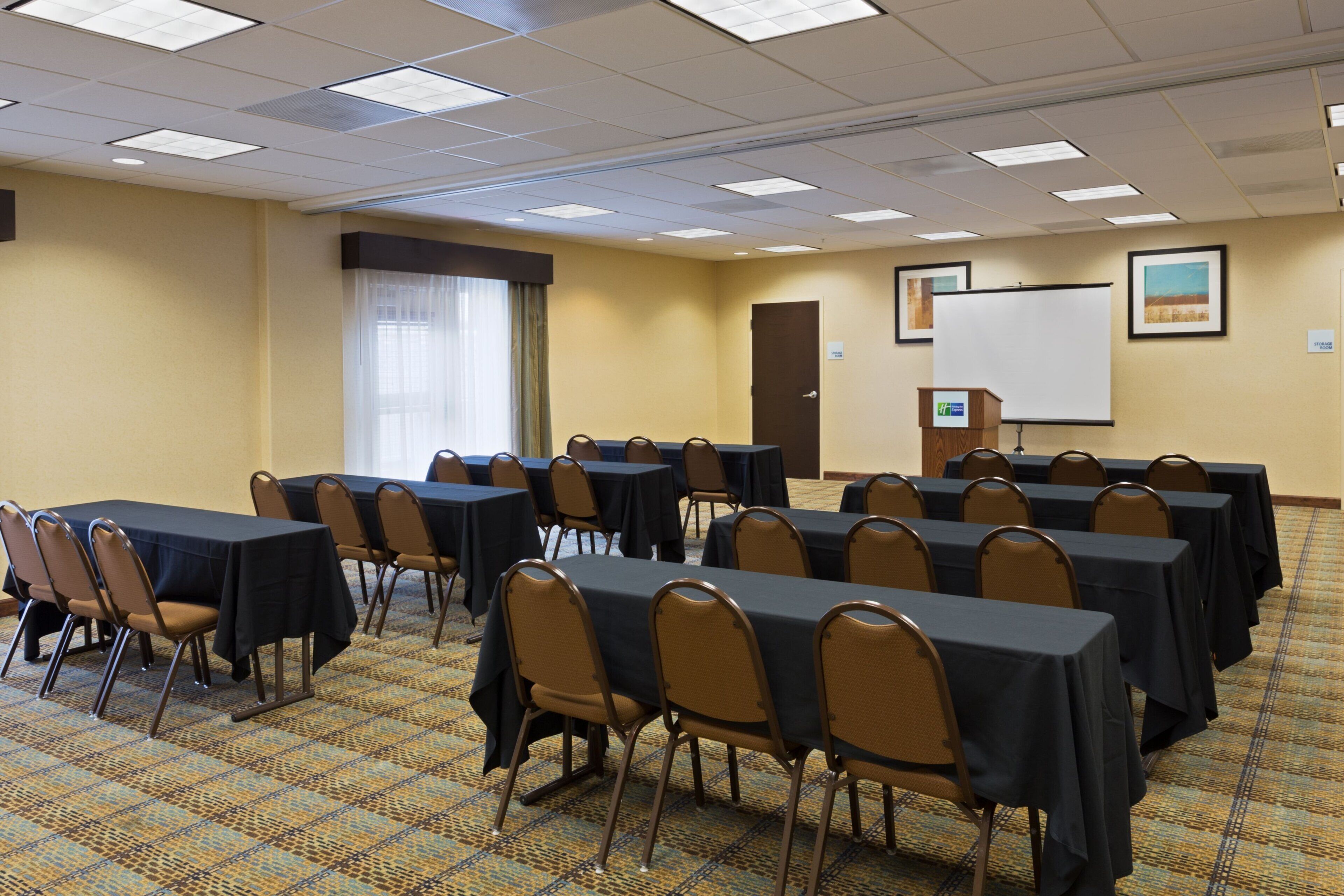 Un salón de conferencias con mesas, sillas, una pizarra y una puerta.