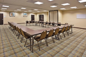 Un salón de conferencias con una larga mesa, sillas, piso alfombrado e iluminación en el techo.