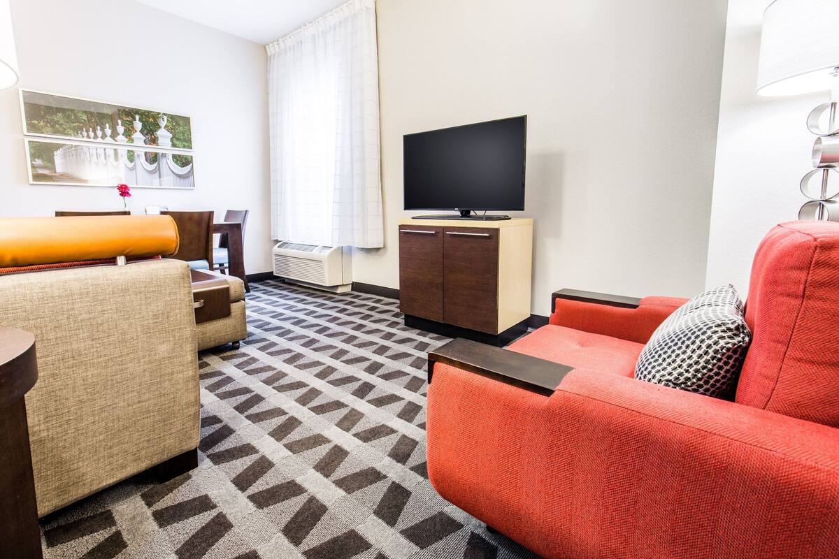 Een moderne hotelkamer met een bank, fauteuil en een flatscreen televisie op een houten kast.