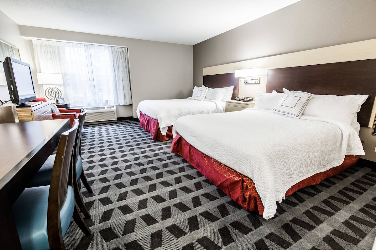 Een hotelkamer met twee bedden, een bureau, een stoel, een televisie en een kamerbreed tapijt met een patroon.