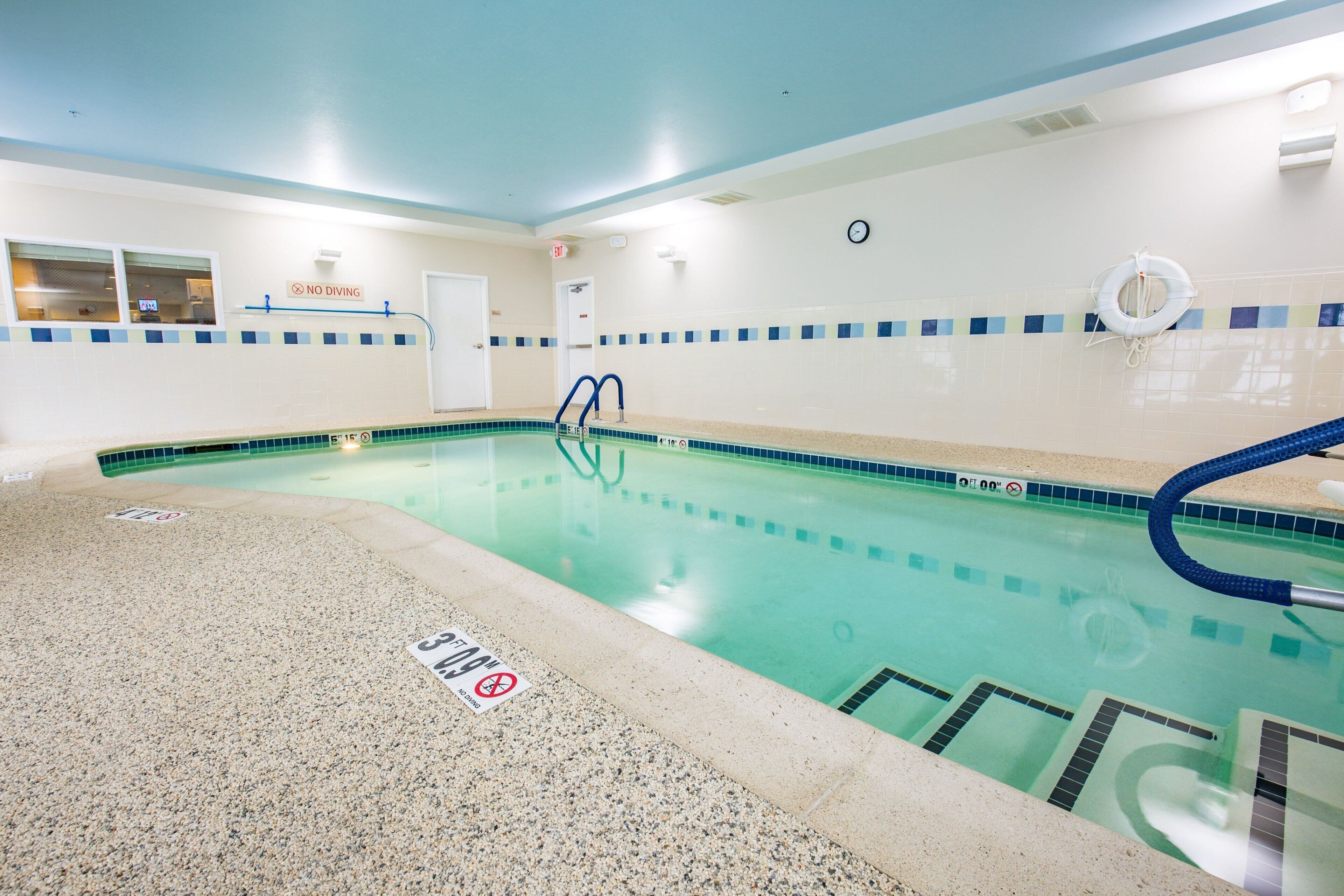 Una piscina interior con carriles delimitados, un cartel de prohibición de buceo y un flotador en la pared.