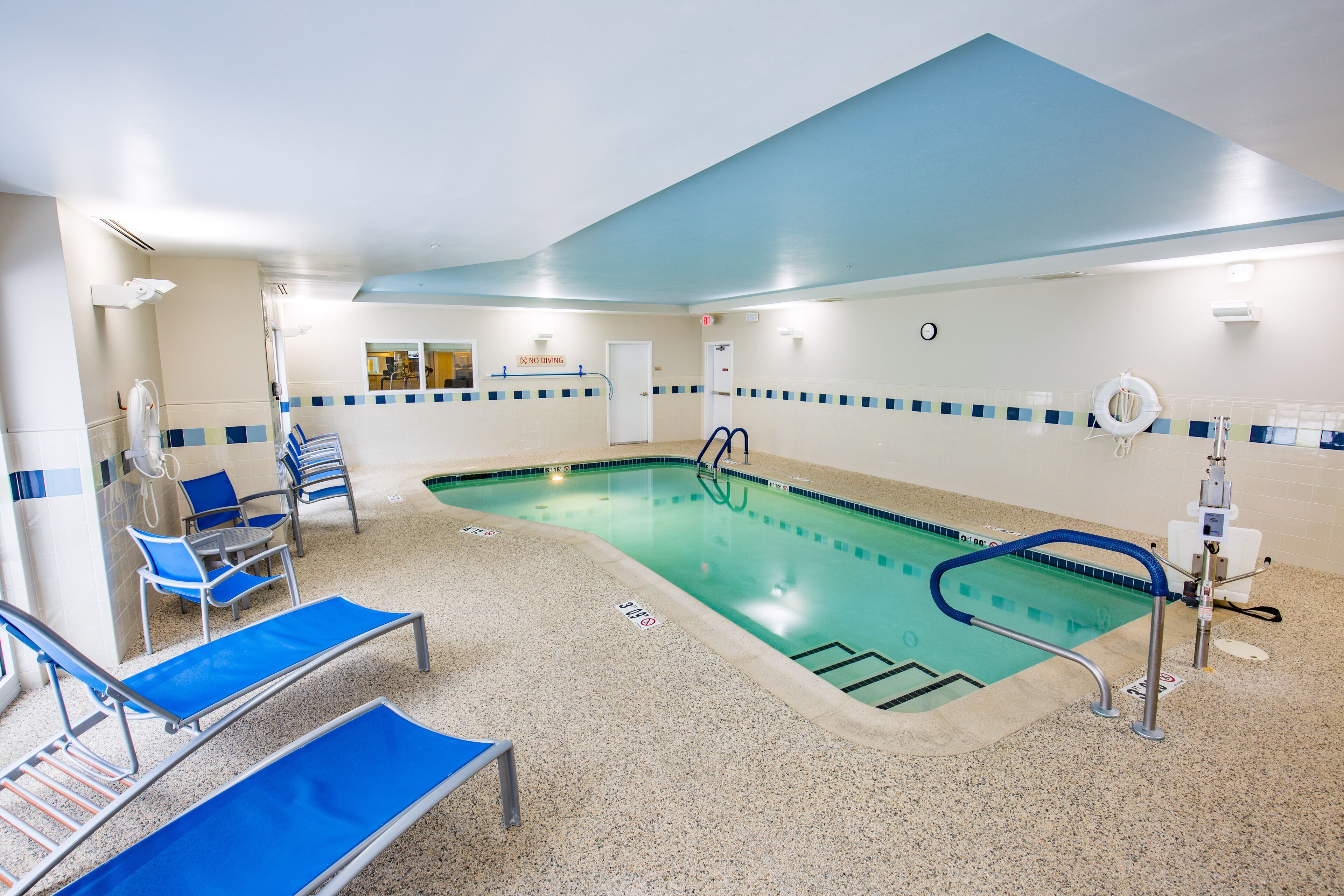 Ein Schwimmbecken mit blauen Liegestühlen und einem Rettungsschwimmerstand.