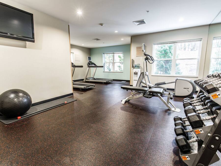 Un gimnasio con cintas de correr, una bicicleta estática y un estante con mancuernas.