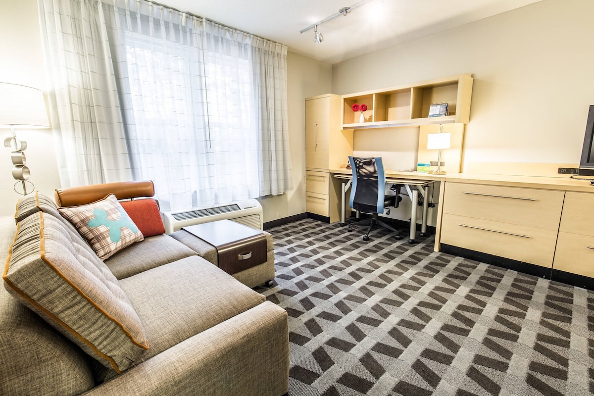 Een hotelkamer met een bank, een bureau, een stoel, een televisietoestel en een kitchenette.