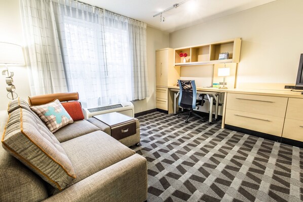 A hotel room with a sofa, a desk, a chair, a television, and a kitchen area. - TownePlace Suites by Marriott Gilford (Gilford)