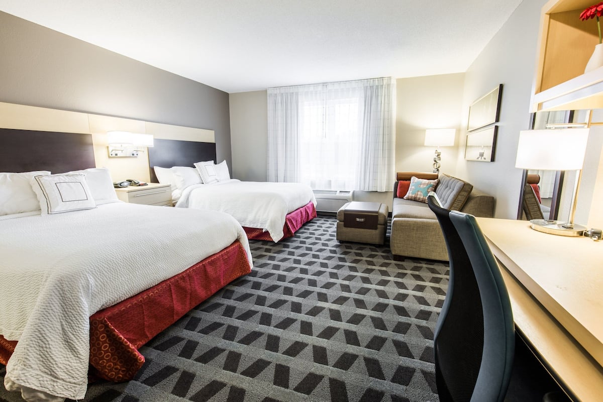 Een hotelkamer met twee bedden, een bureau, een stoel en een groot raam met gordijnen.