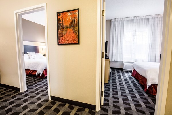 A hotel room with a patterned carpet, a bed with white bedding, a painting on the wall, and a window with curtains. - TownePlace Suites by Marriott Gilford (Gilford)