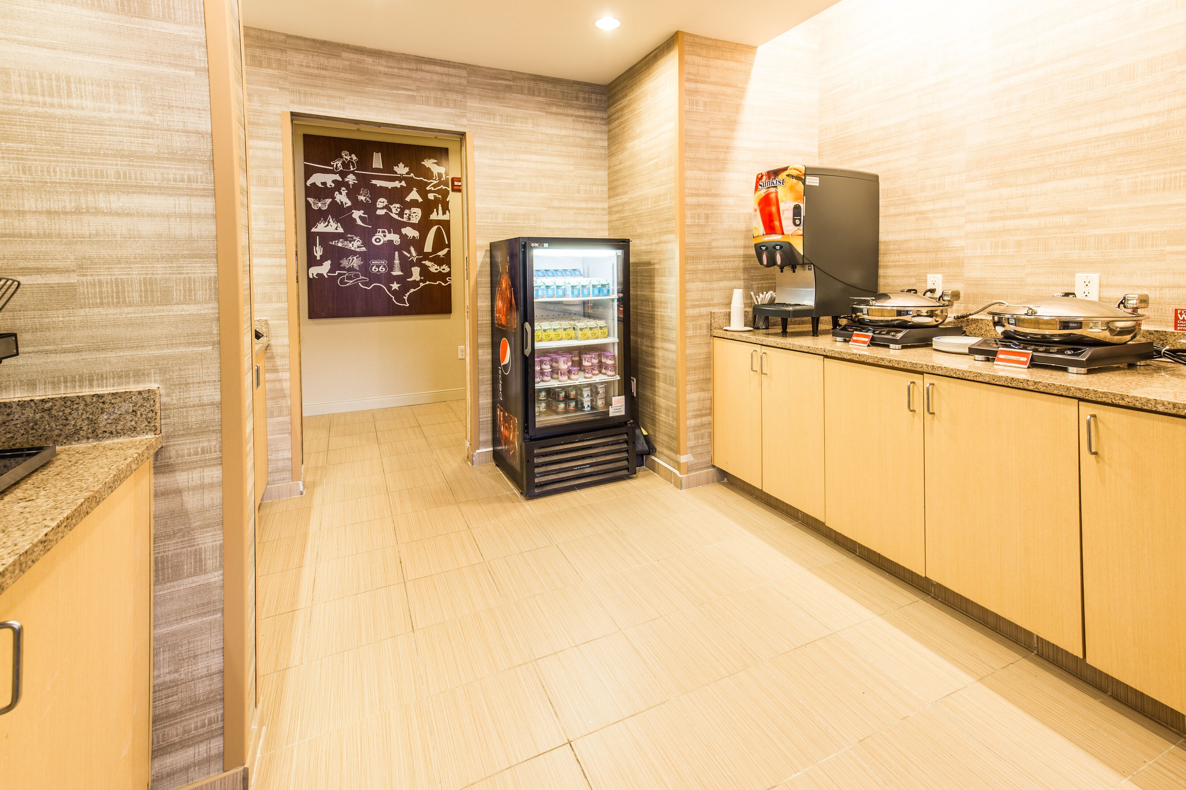 A hotel kitchen with a refrigerator stocked with beverages, a coffee machine, and a microwave.