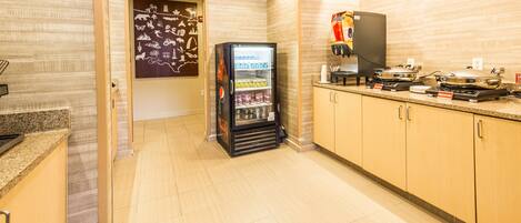 A hotel kitchen with a refrigerator stocked with beverages, a coffee machine, and a microwave.