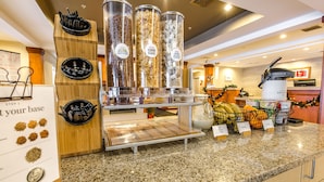 Un comptoir pour le petit-déjeuner avec des distributeurs de céréales, une machine à café et un présentoir de fruits.