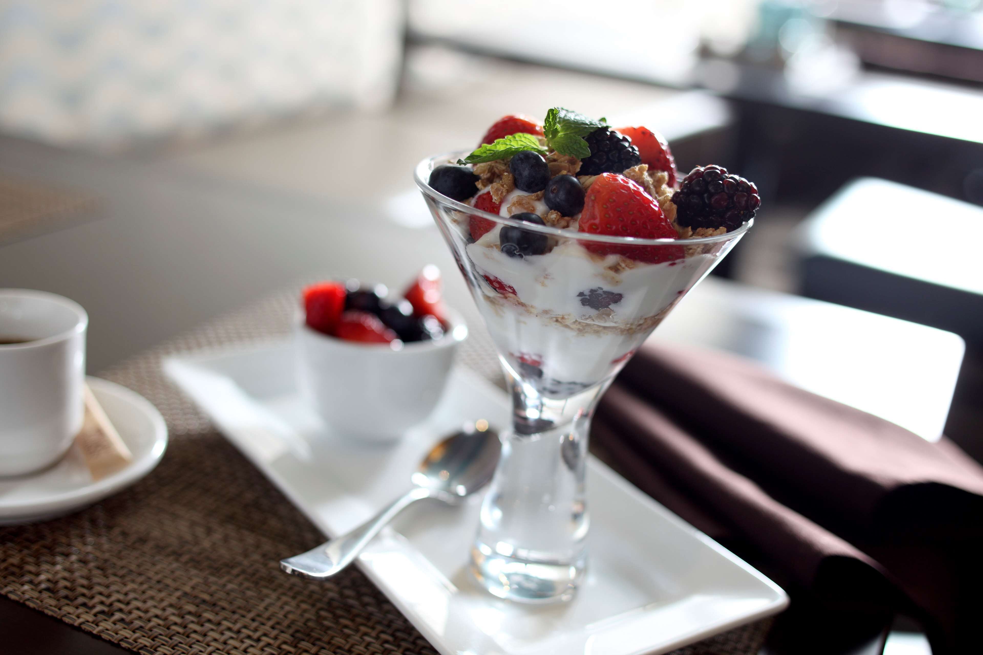 Postre en un bol de vidrio sobre un plato blanco con una cuchara al lado, y una taza de té en un platito a la izquierda.