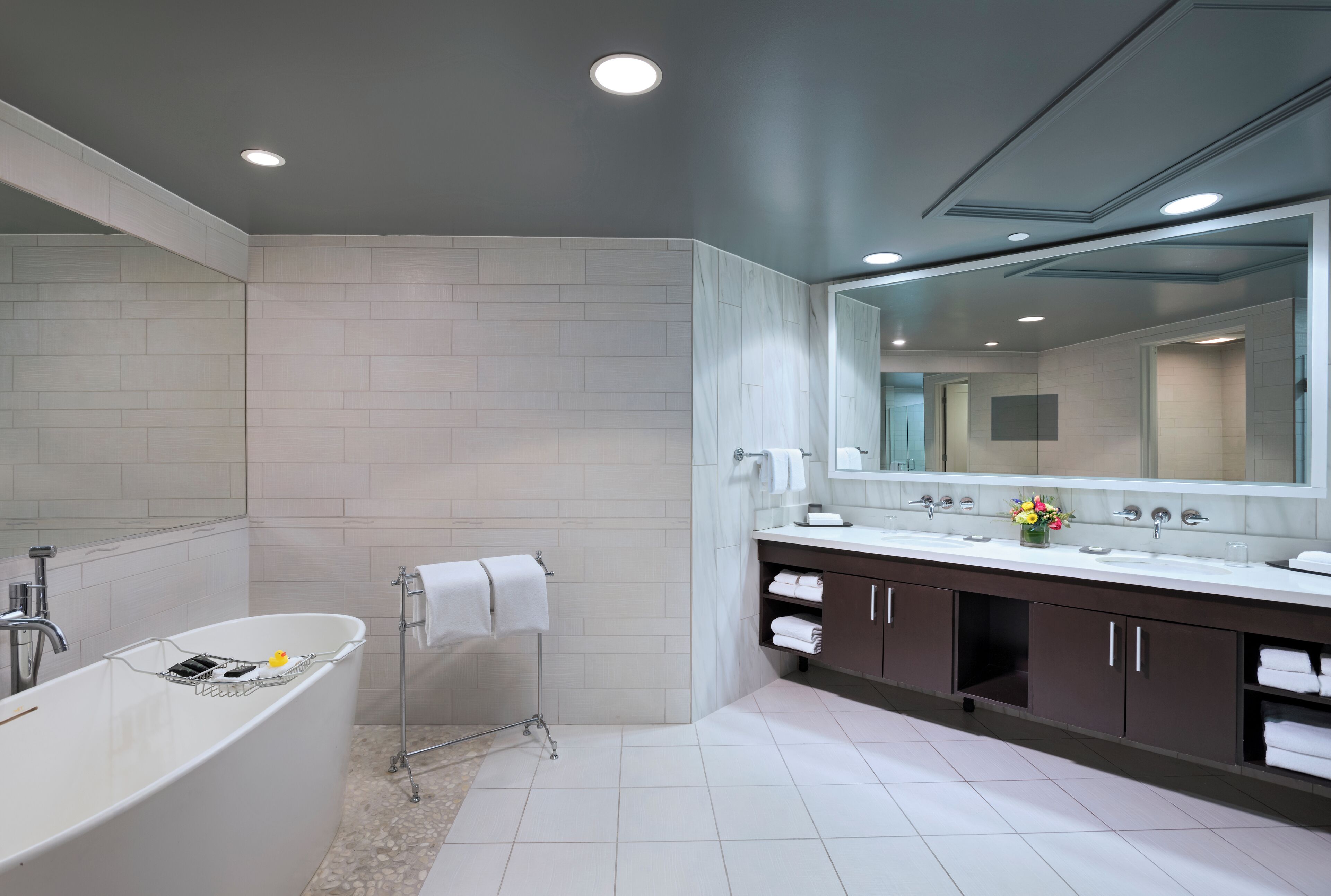 A modern bathroom with a freestanding bathtub, a large mirror, and a vanity with a sink and towel rack.