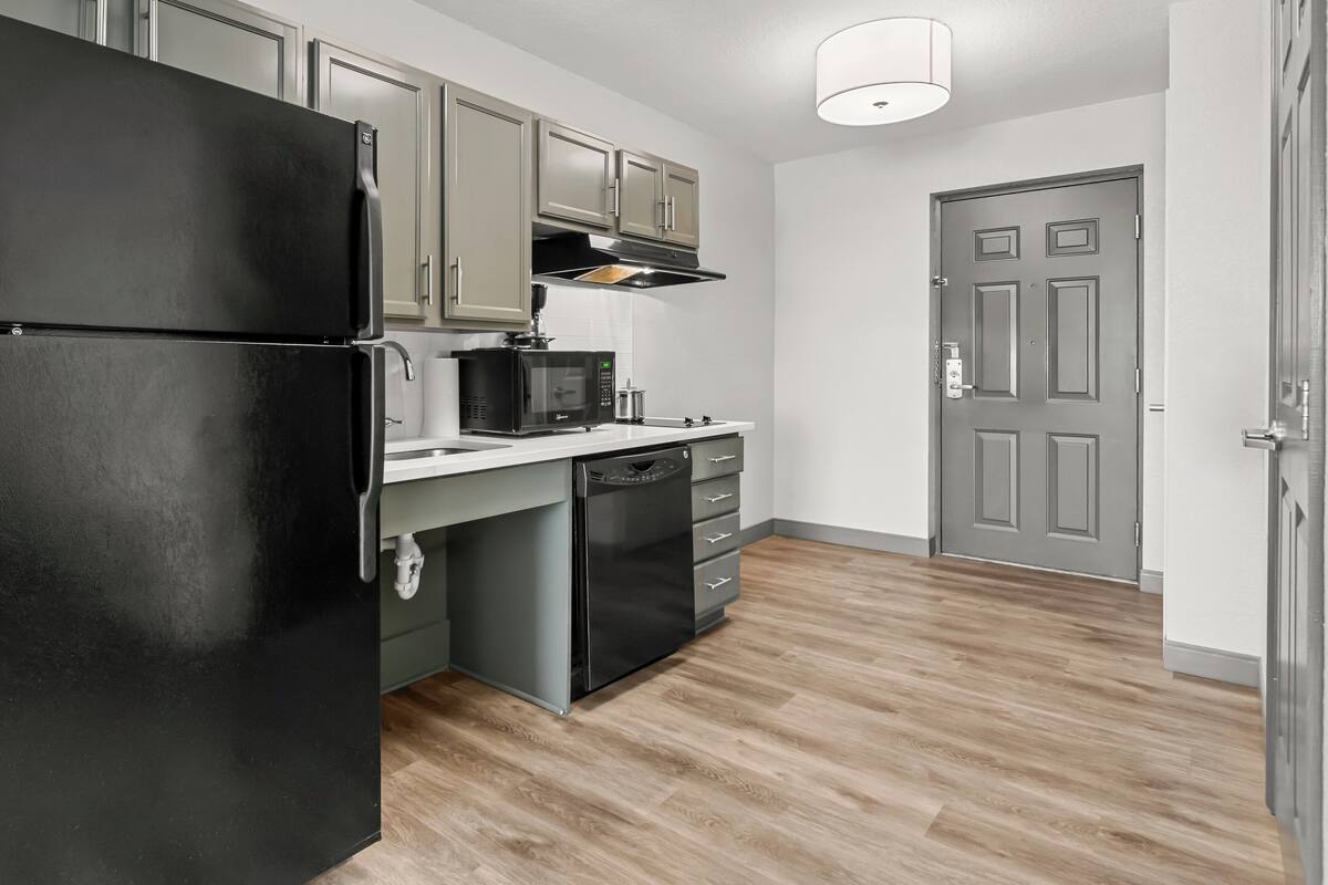Una cocina moderna con un refrigerador negro, microondas, lavavajillas y piso de madera.