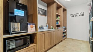 Une petite cuisine équipée d’une machine à café, d’un four à micro-ondes et d’étagères remplies de collations et de boissons.