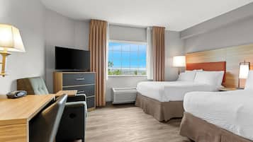 Une chambre d’hôtel équipée d’un bureau, de deux lits, d’une télévision et d’une fenêtre avec des rideaux.