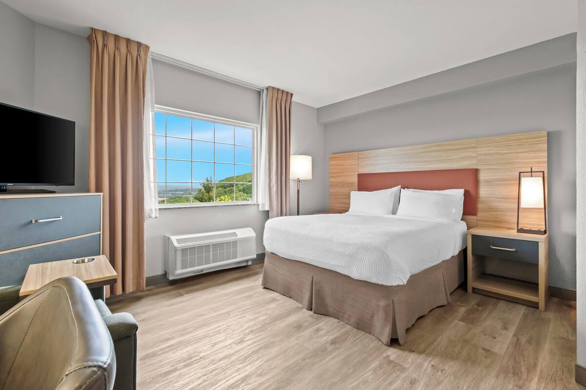 Habitación de hotel con una cama grande, televisor, escritorio y ventana con vistas.