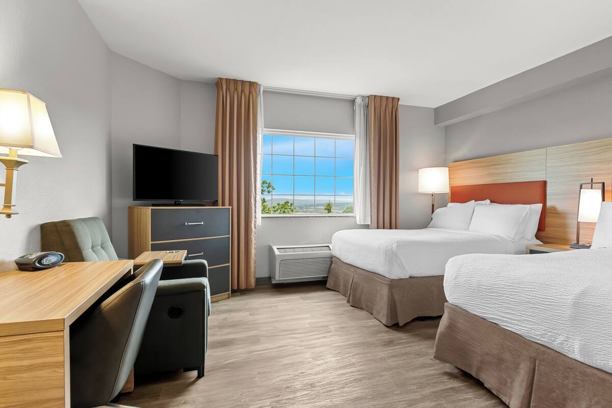 Habitación de hotel con escritorio, dos camas, televisor y ventana con cortinas.