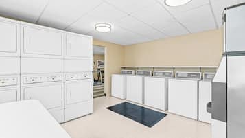 A laundry room with stacked washers and dryers, a black mat, and a ceiling light.