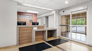 Un espace d’accueil doté d’un comptoir en bois, d’une décoration murale géométrique moderne et d’une grande porte-fenêtre coulissante donnant sur un espace extérieur.