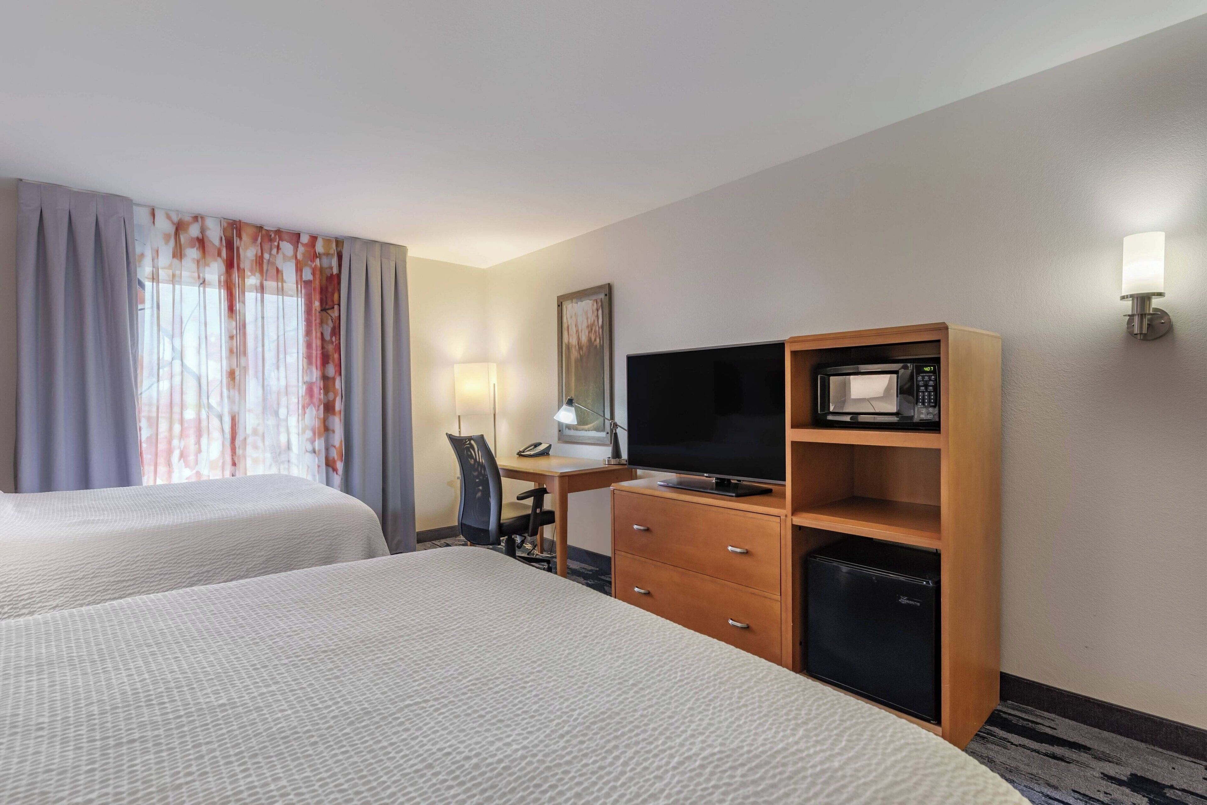 Une chambre d’hôtel avec deux lits, un bureau avec une lampe, une télévision, un four à micro-ondes et un petit réfrigérateur.