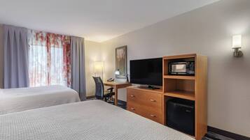 Une chambre d’hôtel avec deux lits, un bureau avec une lampe, une télévision, un four à micro-ondes et un petit réfrigérateur.