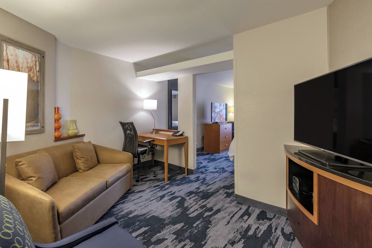 A hotel room with a sofa, desk, TV, and a carpeted floor.