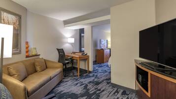 A hotel room with a sofa, desk, TV, and a carpeted floor.