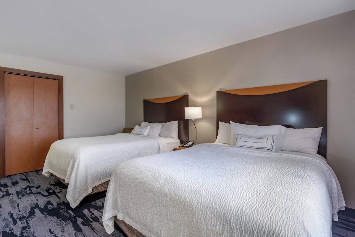 A hotel room with two single beds, a wooden door, a nightstand with a lamp, and a patterned carpet.