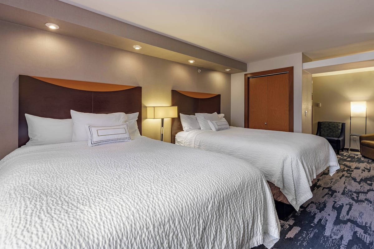 A hotel room with two beds, each with a headboard, a bedside lamp, and a carpeted floor.