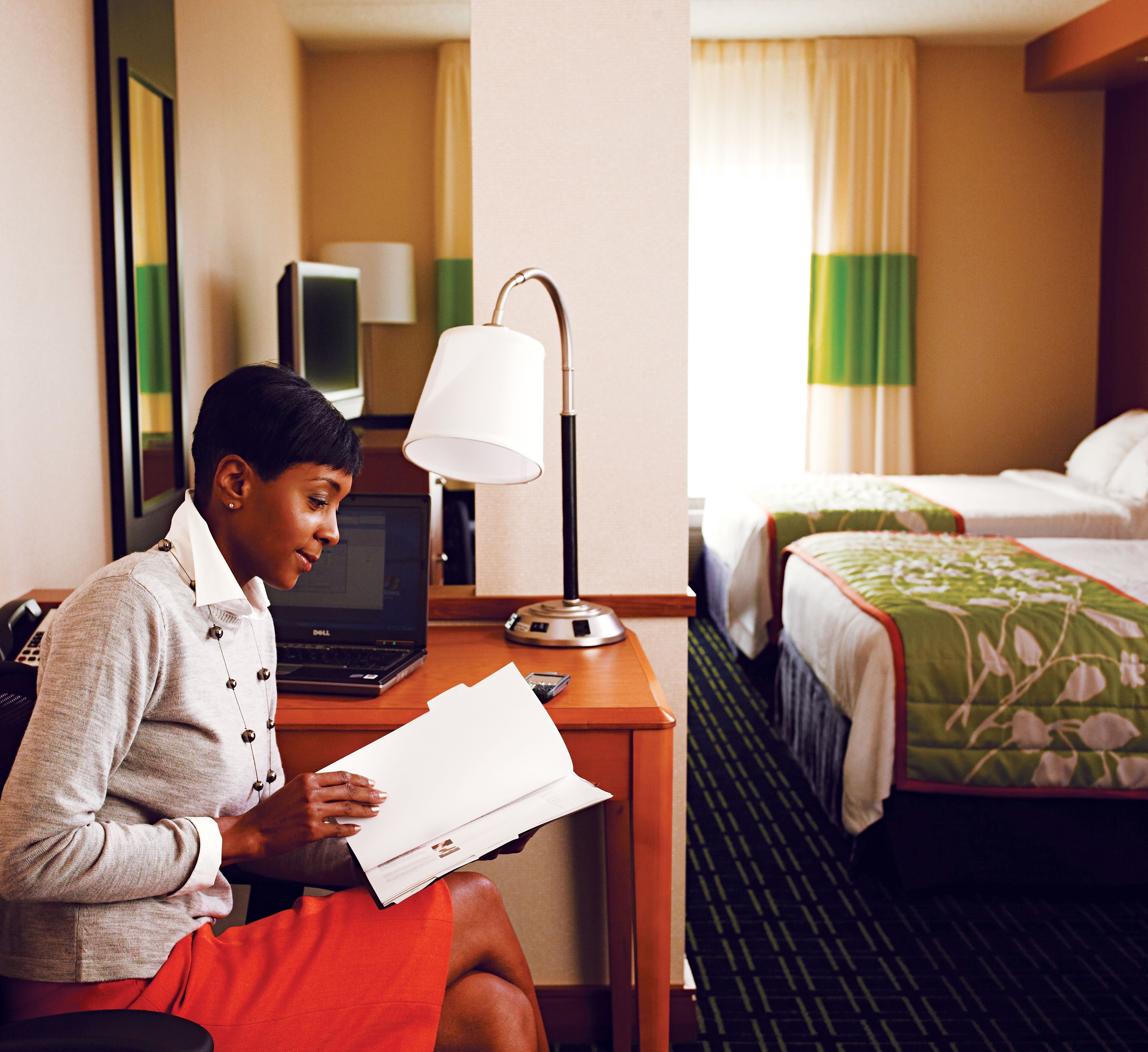 Een hotelkamer met een bureau, een laptop, een lamp en een bed met een bloemenprint beddeken in het groen.