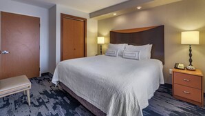 A hotel room with a large bed, bedside lamps, a wooden nightstand, and a bench. - Fairfield Inn & Suites by Marriott Texarkana (Texarkana)