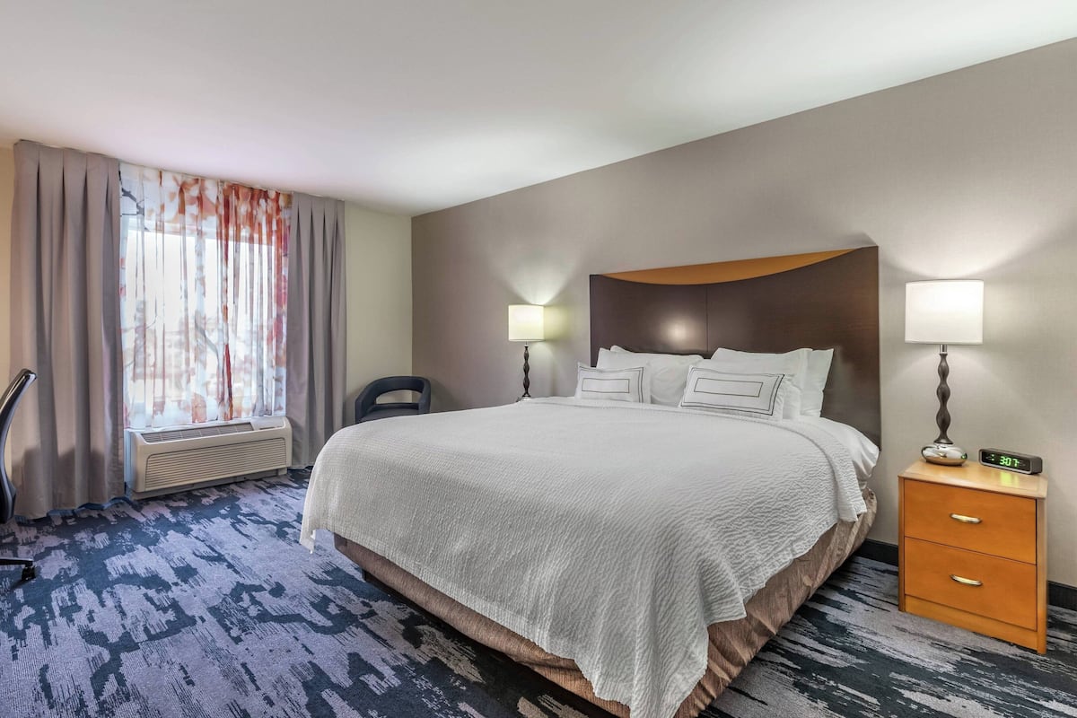 A hotel room with a large bed, two bedside tables with lamps, a chair, and a window with curtains.