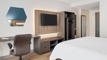A modern hotel room with a bed, desk, chair, TV, and wardrobe.