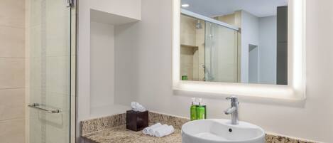 A bathroom with a glass shower enclosure, a sink with a mirror above it, and a countertop with toiletries.