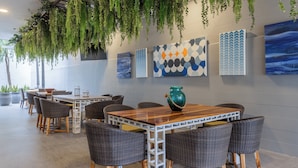 A modern dining area with wicker chairs and a wooden table, surrounded by potted plants and abstract art on the walls. - Holiday Inn Express San Jose Forum by IHG (Pozos)
