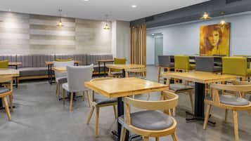 A modern restaurant with wooden tables and chairs, a seating area with cushioned benches, and pendant lighting.