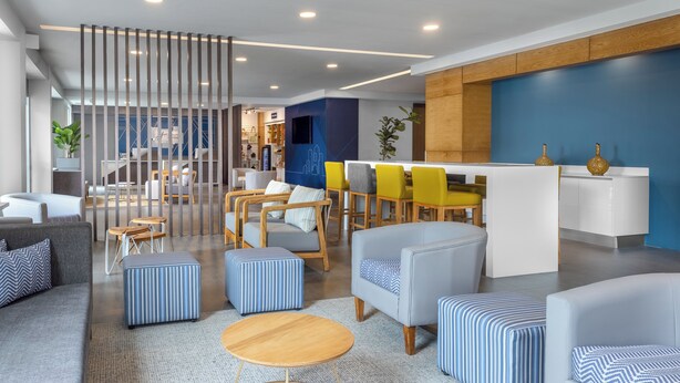 A modern hotel lobby with seating areas, a reception desk, and a partition with vertical lines. - Holiday Inn Express San Jose Forum by IHG (Pozos)
