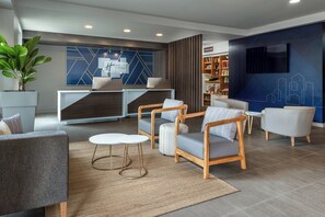 A modern hotel lobby with a reception desk, seating area, and a television screen. - Holiday Inn Express San Jose Forum by IHG (Pozos)