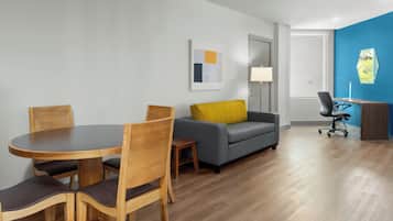 A modern living room with a round wooden table, four chairs, a grey sofa with a yellow pillow, a blue accent wall, and a desk with a chair.