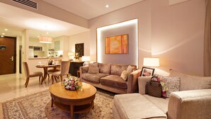 A modern living room with a sofa, armchair, and coffee table, a dining area with chairs, and a kitchen in the background.