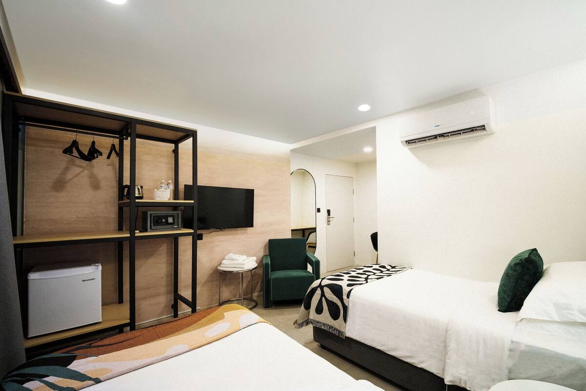 A hotel room with two beds, a TV, a microwave, a chair, and a small table.