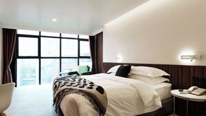 A modern hotel room with a large bed, a bedside table with a phone, and a view of the city through large windows. - Grand Inn Hotel (Bangkok)