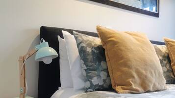 A neatly arranged bedroom with a bed, pillows, a bedside table, a lamp, and a framed artwork on the wall.